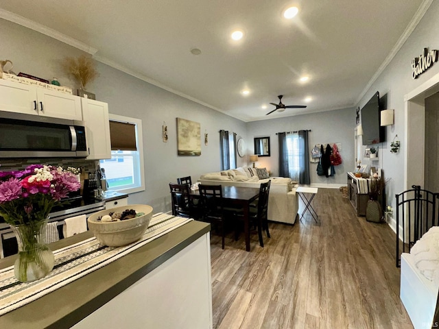 living area featuring light wood-type flooring, plenty of natural light, a ceiling fan, and ornamental molding