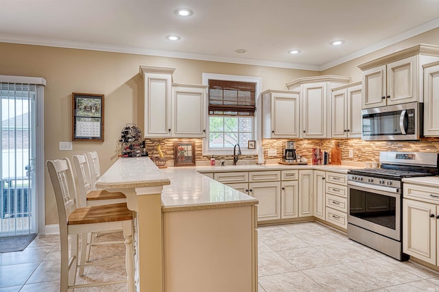 kitchen with cream cabinetry, a peninsula, appliances with stainless steel finishes, and a sink