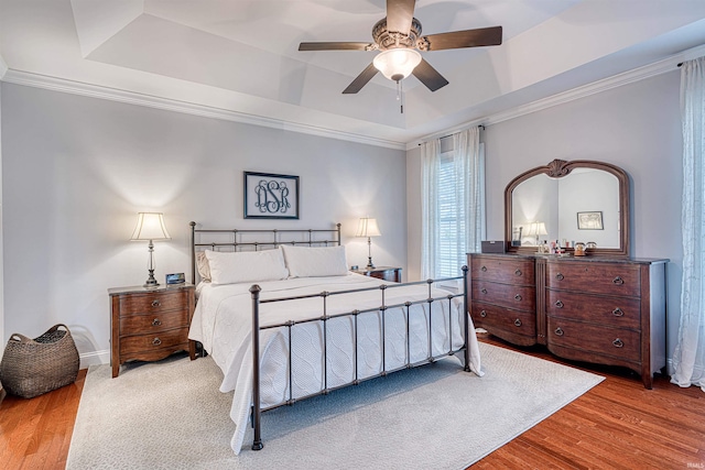 bedroom with a tray ceiling, crown molding, and wood finished floors