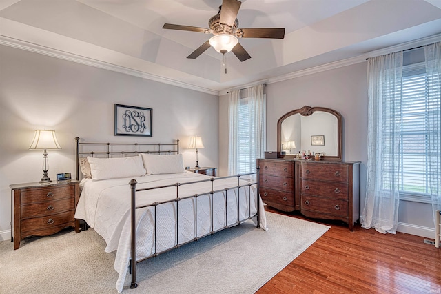 bedroom featuring ornamental molding, a raised ceiling, baseboards, and wood finished floors