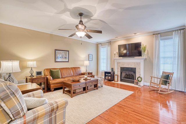 living room featuring a tile fireplace, a ceiling fan, crown molding, light wood-type flooring, and baseboards