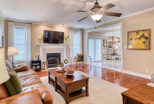 living area with baseboards, ornamental molding, ceiling fan with notable chandelier, and wood finished floors