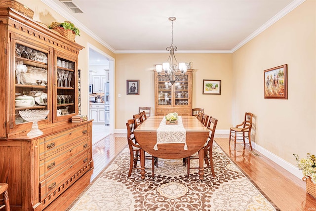 dining space featuring crown molding, light wood-style floors, visible vents, and an inviting chandelier