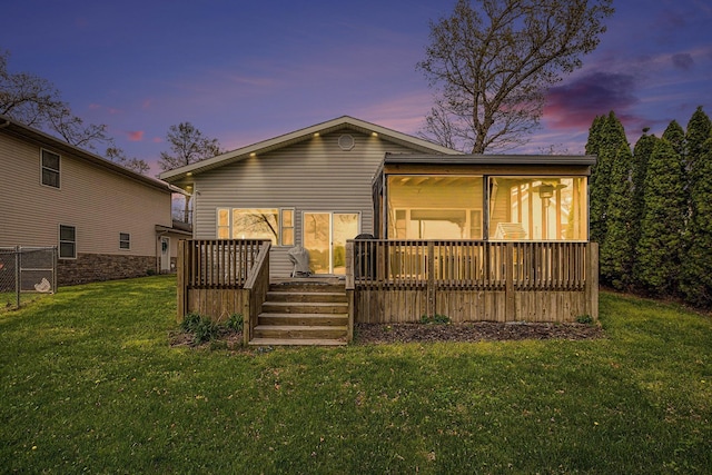 back of house at dusk featuring a deck and a lawn