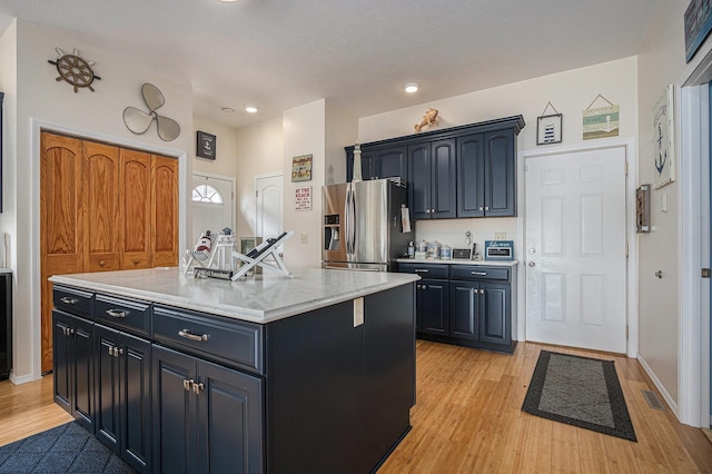 kitchen with stainless steel refrigerator with ice dispenser, light wood-style floors, a kitchen island, dark cabinetry, and recessed lighting