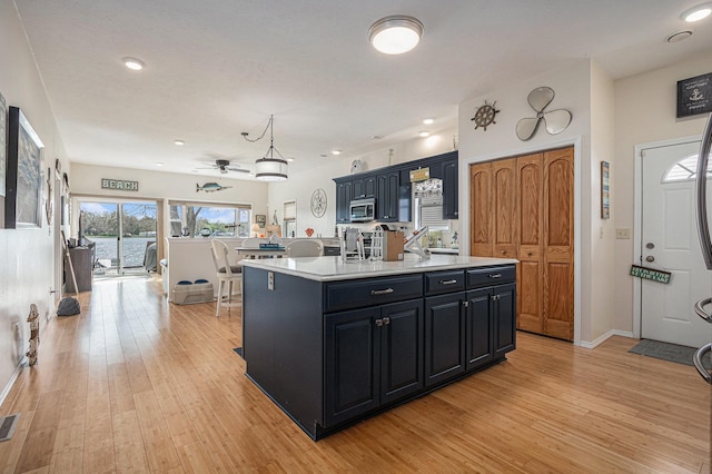 kitchen with a ceiling fan, light wood-style floors, light countertops, and stainless steel microwave