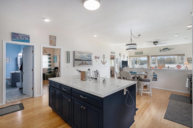 kitchen featuring light wood finished floors, a center island, a ceiling fan, baseboards, and dark cabinetry