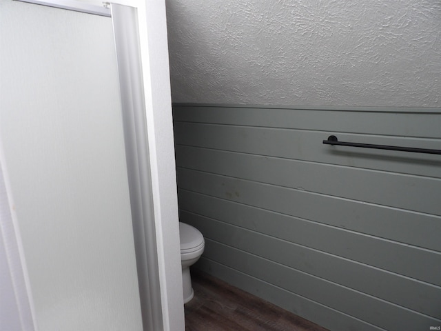 bathroom featuring toilet, wooden walls, a textured ceiling, and wood finished floors