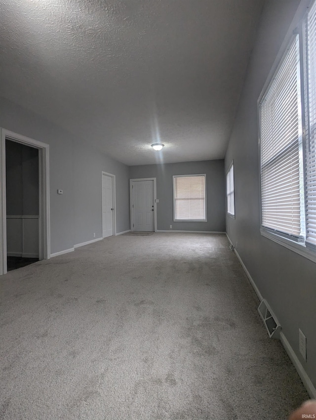 carpeted empty room featuring a textured ceiling, visible vents, and baseboards