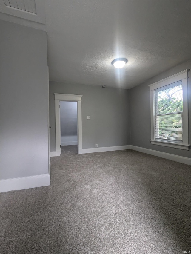 carpeted empty room featuring a textured ceiling and baseboards