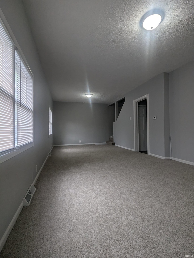 unfurnished room with a textured ceiling, carpet flooring, baseboards, and visible vents
