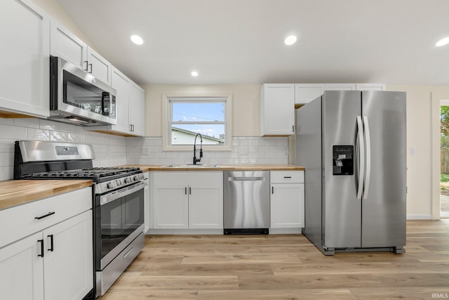 kitchen featuring wooden counters, stainless steel appliances, white cabinets, and a sink