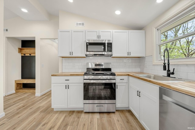 kitchen with vaulted ceiling, stainless steel appliances, butcher block counters, and a sink