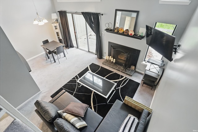 9404 S Lake Ridge Dr, Bloomington, IN 47401 - carpeted living room featuring a fireplace with raised hearth, a chandelier, baseboards, and a towering ceiling