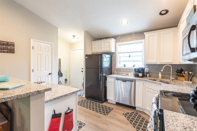 kitchen with a sink, white cabinets, black appliances, light wood-style floors, and tasteful backsplash