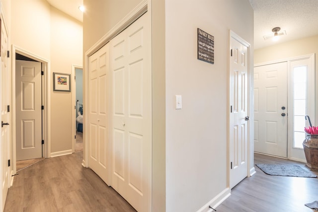 hall with light wood finished floors, visible vents, and baseboards