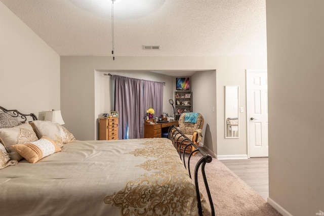 bedroom featuring a textured ceiling, baseboards, visible vents, wood finished floors, and carpet floors