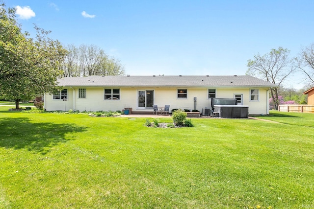 rear view of property with a hot tub, a patio area, and a yard