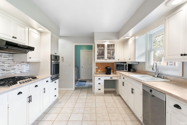 kitchen with stainless steel appliances, under cabinet range hood, a sink, decorative backsplash, and light countertops