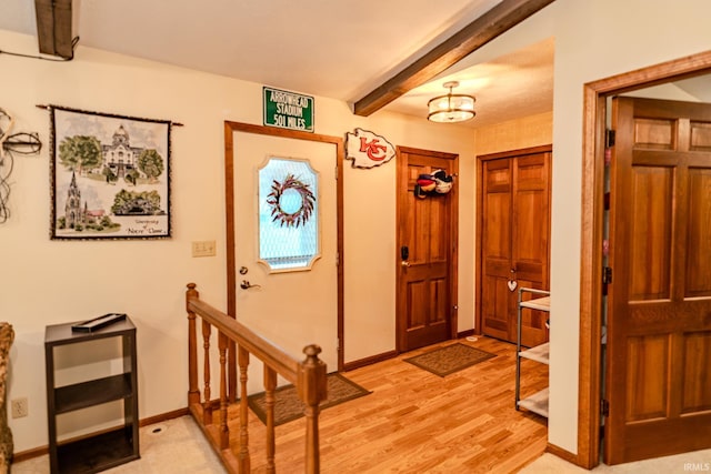 foyer featuring beam ceiling, light wood-style flooring, and baseboards