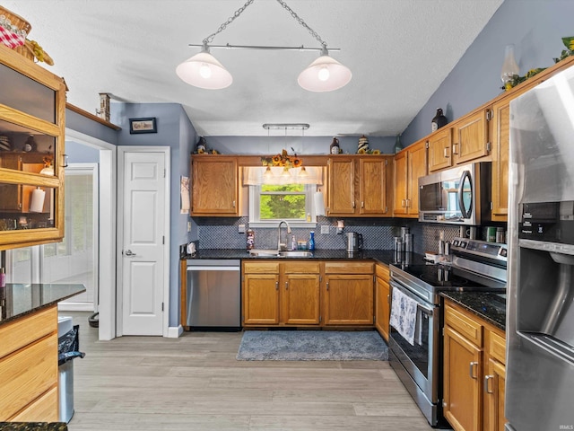 kitchen featuring brown cabinets, a sink, light wood-style floors, backsplash, and appliances with stainless steel finishes