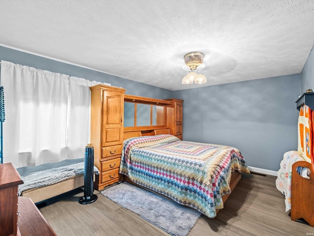 bedroom featuring a textured ceiling, wood finished floors, and baseboards