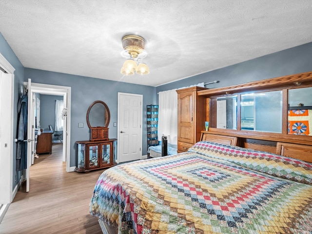 bedroom with light wood-style floors, baseboards, and a textured ceiling