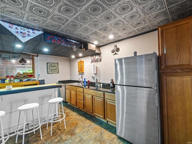 kitchen featuring freestanding refrigerator, dark countertops, an ornate ceiling, and brown cabinets