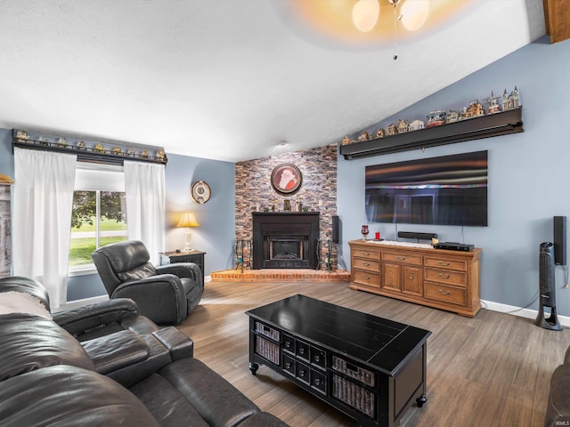 living room with a large fireplace, lofted ceiling, a ceiling fan, and wood finished floors