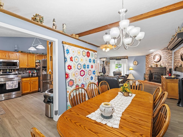 dining area featuring a fireplace, a chandelier, light wood finished floors, and beam ceiling