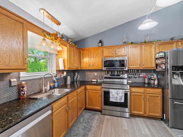 kitchen with a sink, lofted ceiling, appliances with stainless steel finishes, backsplash, and light wood-style floors