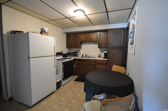 kitchen with a sink, white appliances, dark brown cabinetry, light countertops, and a paneled ceiling