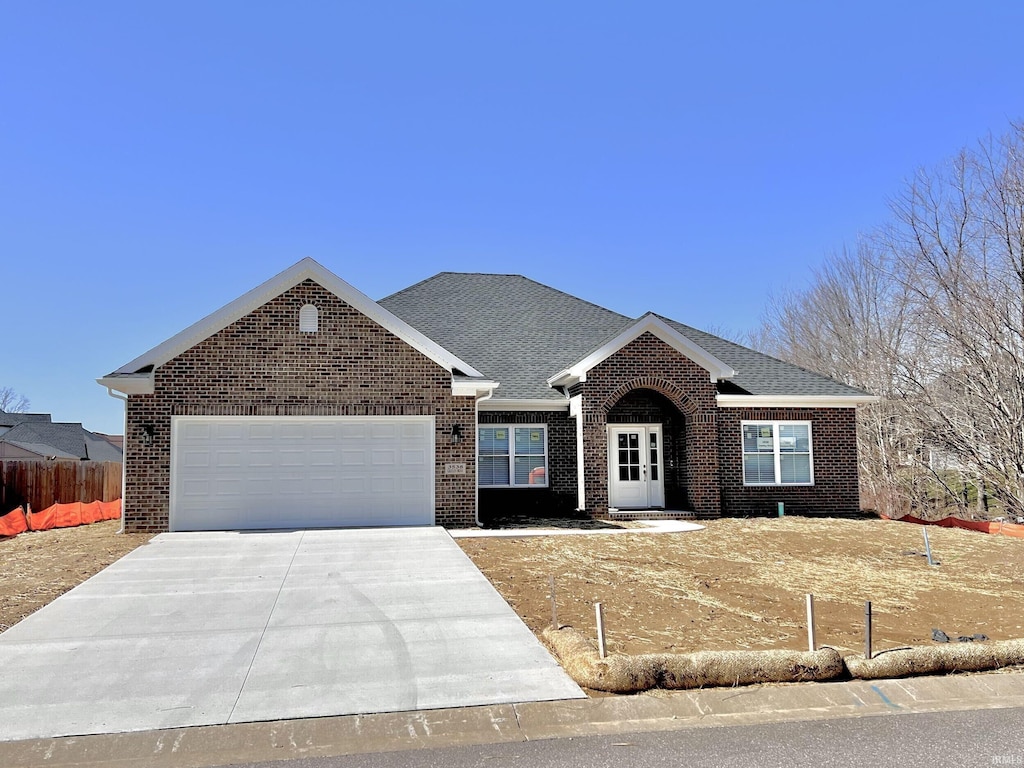 single story home featuring driveway, brick siding, fence, an attached garage, and a shingled roof
