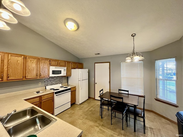 kitchen with a sink, a notable chandelier, white appliances, light countertops, and vaulted ceiling