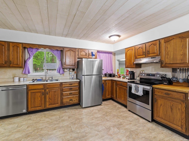 kitchen featuring brown cabinetry, under cabinet range hood, stainless steel appliances, and a sink