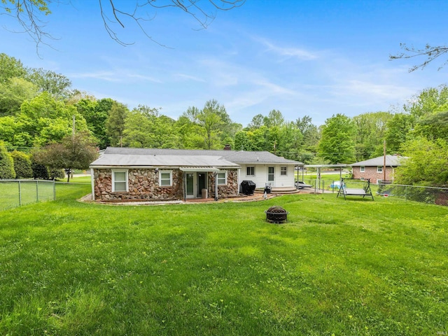 back of property with stone siding, a fenced backyard, a chimney, a lawn, and an outdoor fire pit