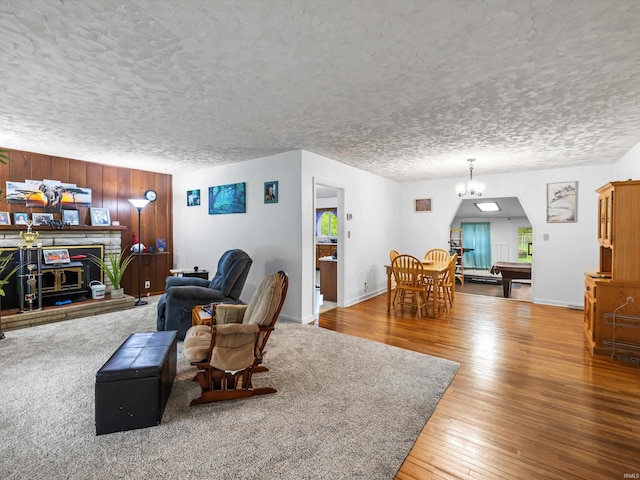 living area featuring a textured ceiling, an inviting chandelier, hardwood / wood-style flooring, arched walkways, and a fireplace