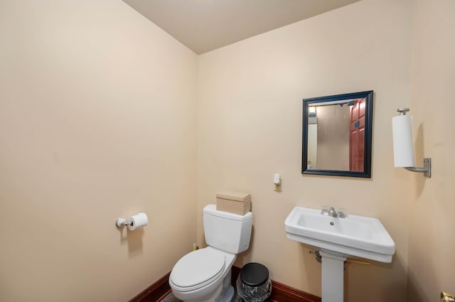 bathroom featuring toilet, baseboards, wood finished floors, and a sink
