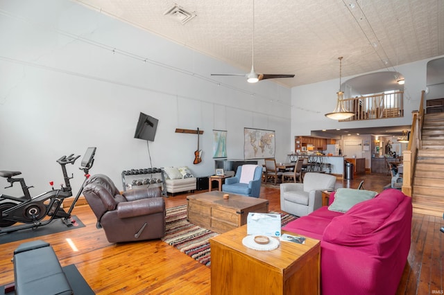 living area with a ceiling fan, hardwood / wood-style floors, a towering ceiling, and stairway