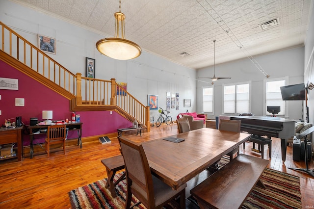 dining area featuring a ceiling fan, wood-type flooring, visible vents, crown molding, and stairway
