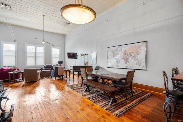 dining room with hardwood / wood-style flooring, a high ceiling, a ceiling fan, and visible vents