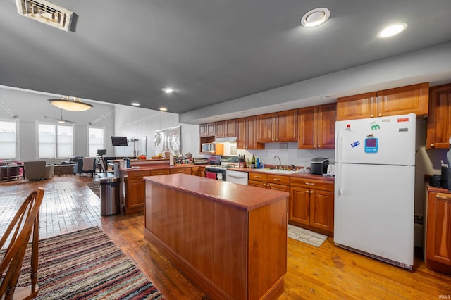 kitchen with light wood-type flooring, brown cabinetry, a sink, and white appliances