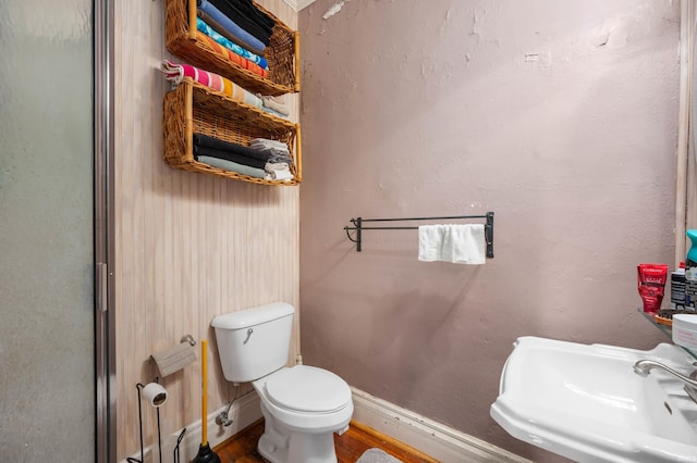 bathroom featuring toilet, baseboards, wood finished floors, and a sink