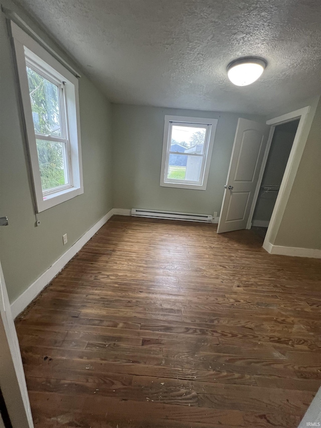 712 E Water St, Portland, IN 47371 - unfurnished bedroom with a textured ceiling, dark wood finished floors, multiple windows, and a baseboard heating unit