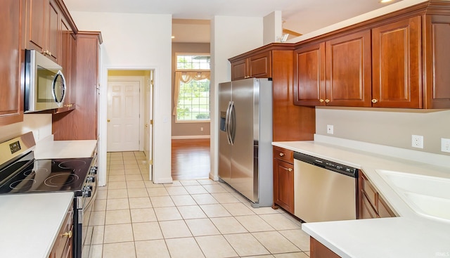 kitchen featuring stainless steel appliances, light tile patterned floors, brown cabinetry, a sink, and light countertops
