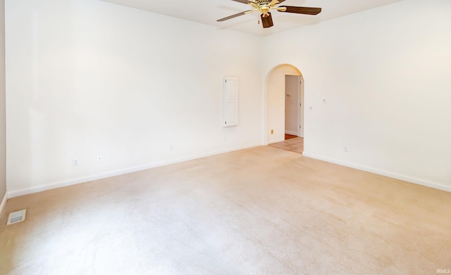 spare room with light colored carpet, visible vents, ceiling fan, arched walkways, and baseboards