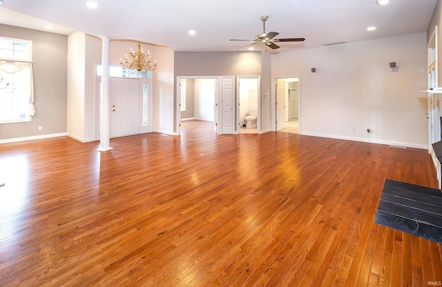 unfurnished living room with a wealth of natural light, light wood-style flooring, and ceiling fan with notable chandelier