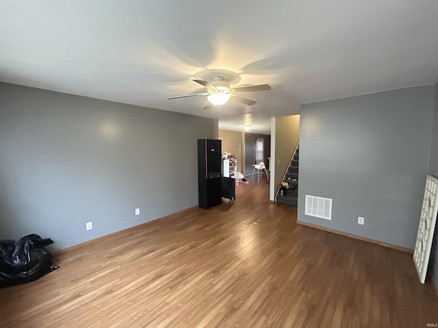 unfurnished living room featuring visible vents, wood finished floors, a ceiling fan, and stairway