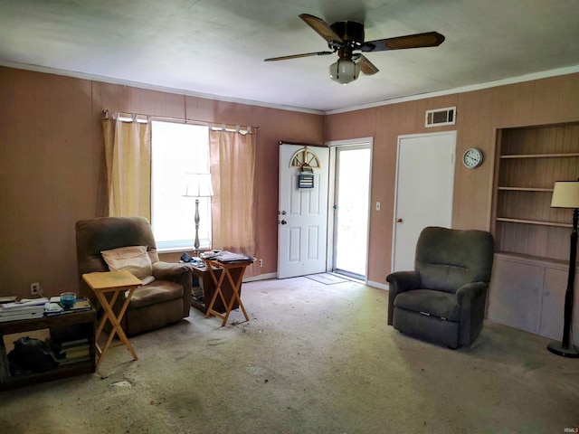 living area with a wealth of natural light, wooden walls, ceiling fan, and visible vents