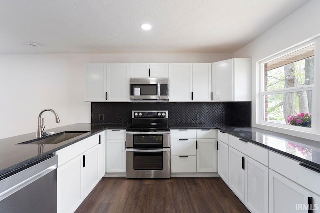 kitchen with a sink, white cabinetry, dark wood-style flooring, appliances with stainless steel finishes, and tasteful backsplash